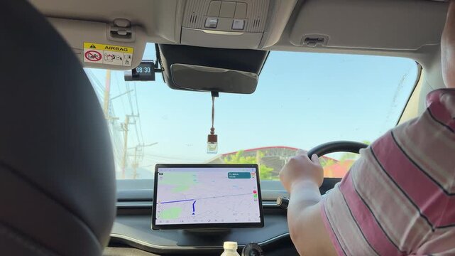 East Asian man driving and checking GPS map during the day.
