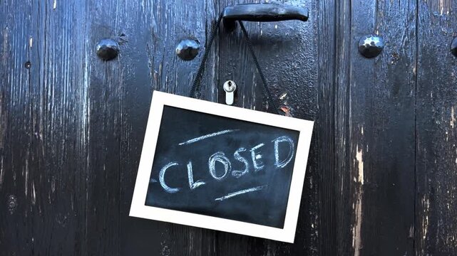 Chalkboard sign with the word CLOSED hanging on an old wooden door handle. Concept for business closure, traditional shops, holidays, or temporary shutdown.