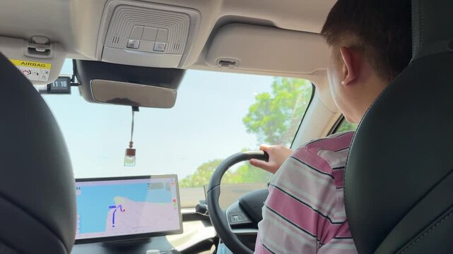 East Asian man driving and checking GPS map during the day.