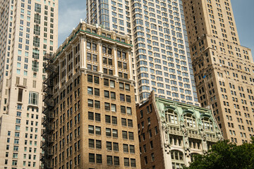 Historic brick buildings stand in front of modern glass and steel skyscrapers in Lower Manhattan, New York City. The financial district architecture shows a strong contrast between classic and