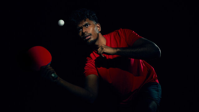 Table tennis player tracking ball during high speed rally in dark arena style lighting. Concept of professional competition, reaction speed metrics, performance analysis, high level sport training.