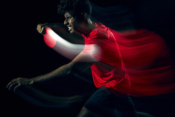 Obraz premium Table tennis player with dynamic motion blur showing rapid movement in dark studio. Concept of fast paced gameplay, high speed reaction, athletic performance and modern sports visual storytelling.