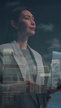 Vertical Screen. Asian Businesswoman in a Light Blazer Stands by an Office Window, Reviewing a Tablet, Looking at Big City Opportunities. Continuing Digital Work With Focus and Determination