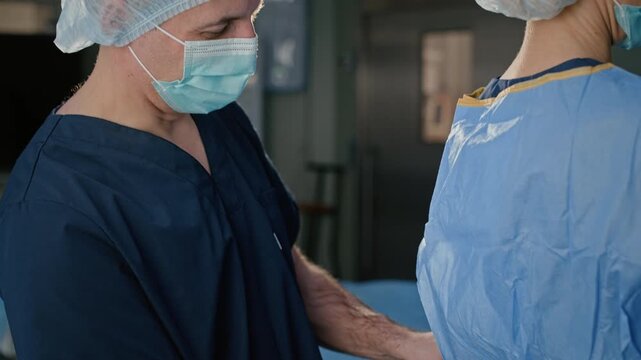 Male anesthetist having small talk with surgeon while helping her with sterile gown before operation