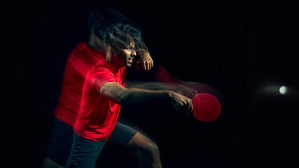 Fototapeta premium Table tennis player reacting to fast ball with motion blur in dark studio. Concept of reaction speed training, reflex development, quick response ability and athletic performance improvement.