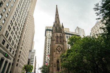 A historic Gothic church stands between tall skyscrapers in Manhattan New York. The stone facade and spire contrast with surrounding modern office buildings in the busy urban city center.