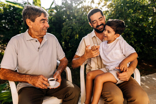 Grandfather, adult son and young grandson sitting outdoors and interacting with affection, representing family bonding and multigenerational connection.