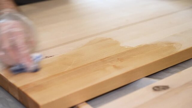 Hand applying wood protection oil on boards with rags. Hand applying wood protection piece in gold color with rags, indor. Impregnation of wood and coating with oil