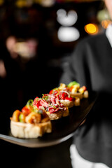 A waiter holding a black platter with three different types of gourmet bruschettas. Close-up on the...