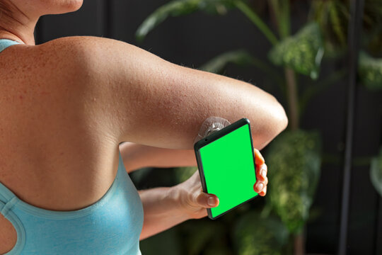 Diabetic young woman with glucose sensor and mobile phone measuring blood sugar level at home