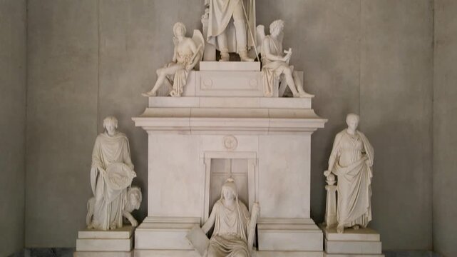 Camera pans upward inside a marble monument at Quinta de San Pedro Alejandrino, revealing white statues on a tiered pedestal and a red velvet rope barrier.