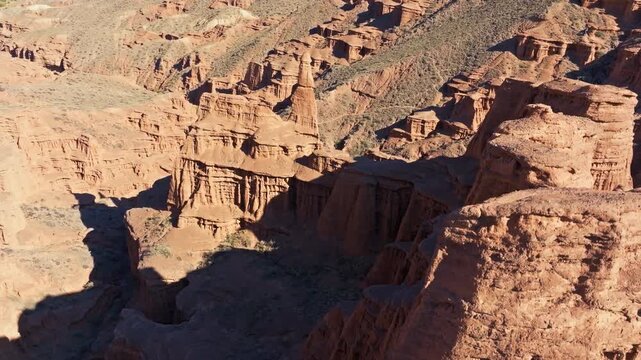 Descending aerial view captures unique geological formations and canyons in Kyrgyzstan. The arid landscape showcases natural rock formations under daylight.