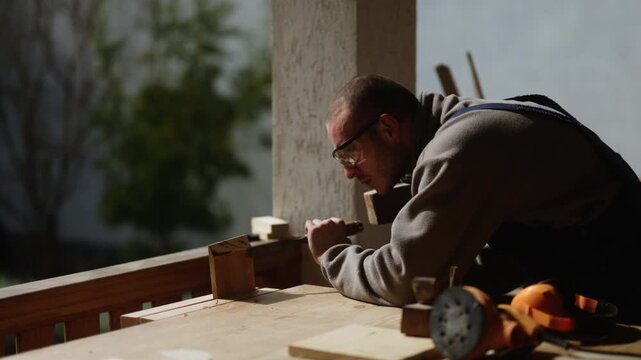 A dedicated carpenter meticulously chisels a piece of wood, focusing on traditional craftsmanship. This skilled artisan demonstrates woodworking precision using classic hand tools outdoors.