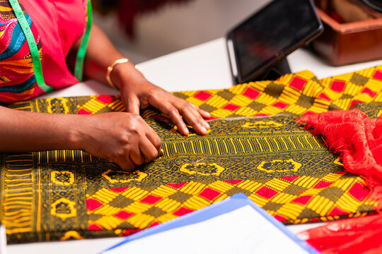 African tailor's hands marking colorful ankara fabric with chalk on a workspace