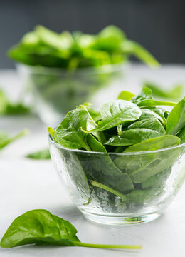 Spinach in a transparent glass bowl on gray background with reflection. Heap of Baby spinach fresh leaves close up, water drops, Healthy vegan food, diet, dieting, vitamin, vertical image