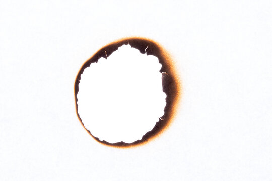 Paper sheet with irregular burnt hole and dark scorch marks