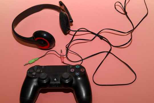 Lviv, Ukraine - March 19, 2026: ​A black wireless controller and a wired headset with a microphone lie on a pleasant pink background, creating a stylish set for a gamer.