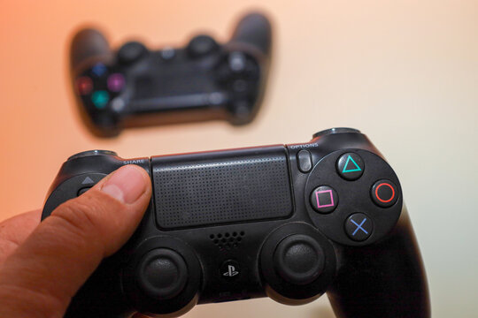 Lviv, Ukraine - March 19, 2026: A hand holds a black DualShock gaming controller in the foreground, focusing on the buttons and touchpad area.