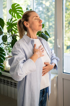 Mindful woman with hands on chest and abdomen practicing deep breathing, calming meditative exercise for stress and anxiety relief, self care in everyday life, female using controlled breathing.
