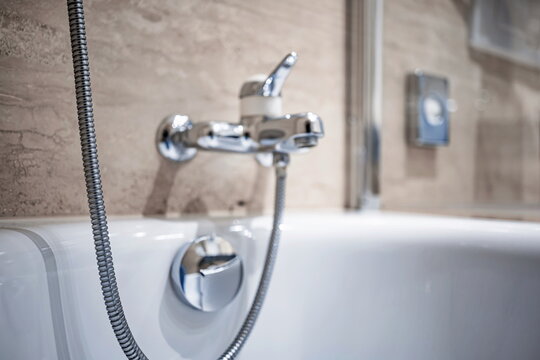 Blurry or blurred background of a modern chrome bathtub faucet and shower hose in a bright bathroom