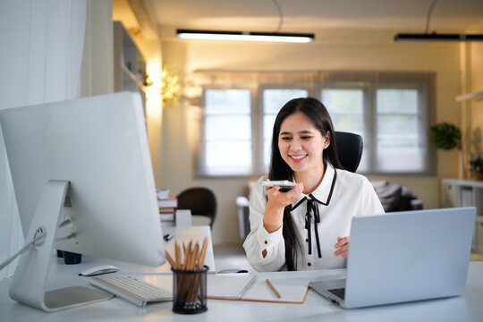 female work by laptop dictate audio message speech on mobile phone voice recording application. Young woman freelance worker talk to client using loudspeaker send voicemail via cell inside office
