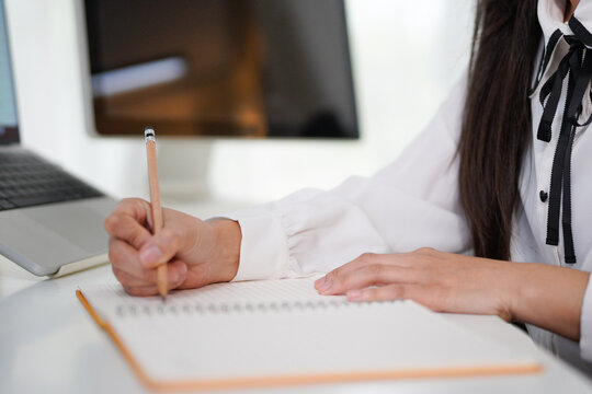 Corporate asian woman, notebook and writing in planning, schedule or strategy for job as receptionist. Woman, professional and laptop on table by book, working or thinking of idea for research notes