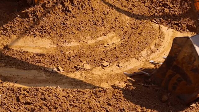 Heavy duty yellow JCB excavator bucket lifting and moving fresh brown soil to level the ground at a residential construction site or plot development project.
