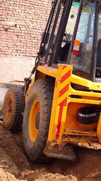 Close up shot of a JCB excavator's heavy-duty yellow wheel moving on fresh loose soil, leveling the ground at a residential construction site or plot.
