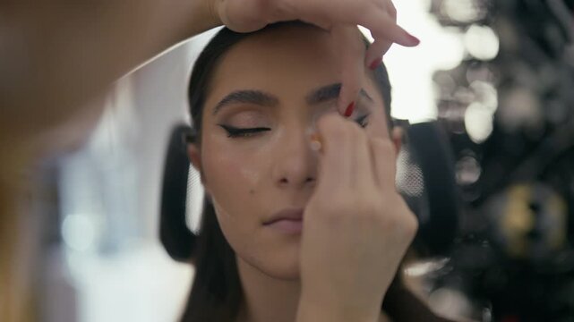 A professional makeup artist meticulously applies false eyelashes to a young woman's eyes. Close-up of an aesthetician enhancing a client's beauty in a salon setting.