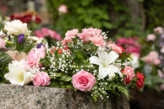 Funeral flower arrangement of red and white flowers. Beautiful funeral flowers on a memorial stone in a cemetery. August day after rain. Blurred background.