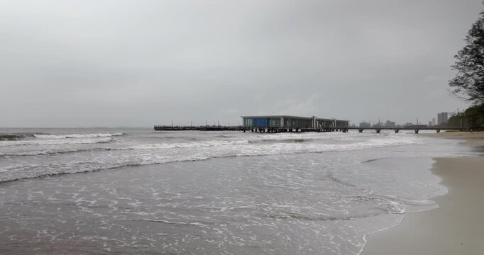 Slow motion view of waves rolling toward a modern pier with a helipad on an overcast day.