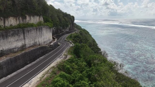 Aerial drone view of a winding road along a steep coastal cliff overlooking the sea.