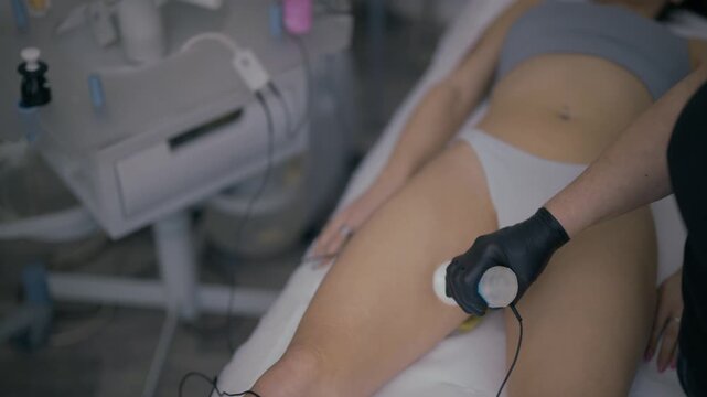 A professional applies a cosmetic device for body contouring on a woman's thigh in a beauty salon. This aesthetic procedure aims for skin rejuvenation and anti-cellulite effects.