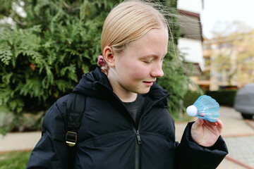 Teen girl holding shuttlecock outdoors in residential yard, examining sports equipment, curiosity, learning, leisure activity, active lifestyle, focus, concentration, childhood, everyday life.
