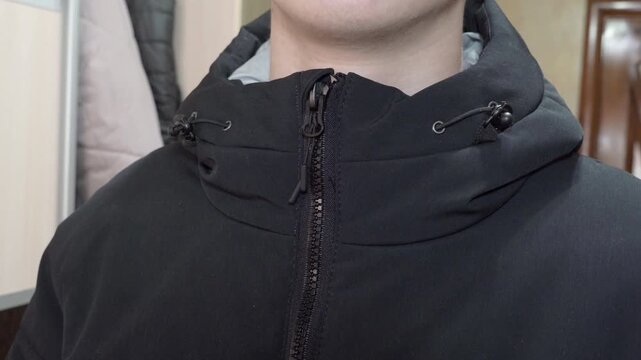 Man buttoning up black hooded jacket, Hand fastens zipper on black outerwear