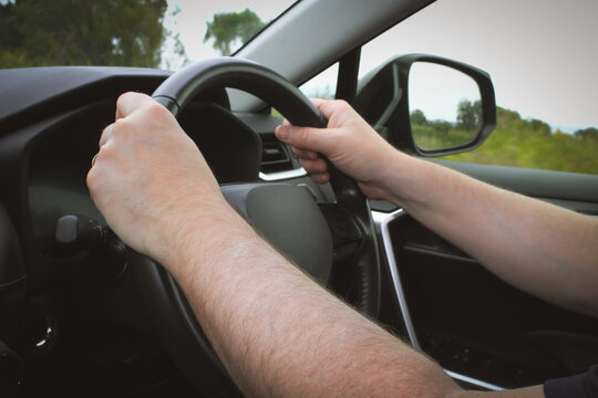 Closeup of a person with their hands on the steering wheel driving in a Right Hand Vehicle RHD (Right Hand Drive). Transportation, safety and commuting themes.