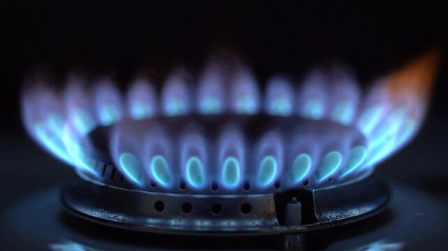 Blue flames of gas burner ignite in sequence, showcasing the vibrant glow in a dark kitchen setting. Concept of rising oil prices, energy market volatility, fuel cost increase, inflation