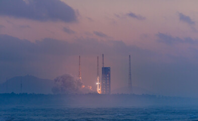 Fototapeta premium Rocket launch at dawn with smoky cloud trail and soft horizon. Launcher with space shuttle in Wenchang Hainan, aerospace program of China.