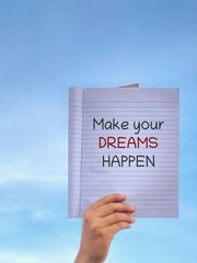 Motivational quote make your dreams happen on notebook held outdoors symbolizing ambition determination and success mindset.