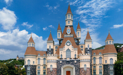 Fototapeta premium Enchanting castle with turrets and clock under blue sky and clouds, amusement park island in Nha Trang, Vietnam at sunset