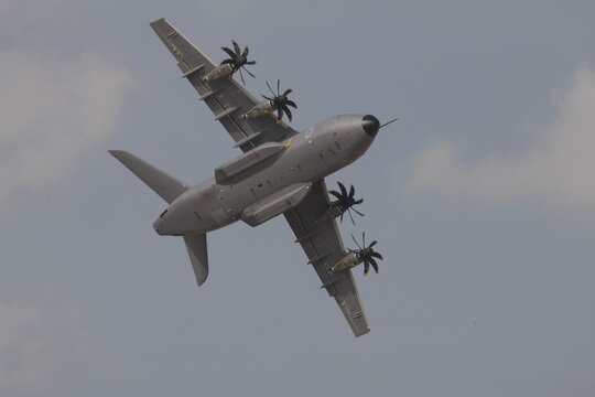Airbus A400M Atlas military transport aircraft performing a steep banked turn against a cloudy sky during an aerial flight display.