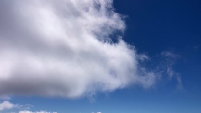 A single cloud gently floating across a clear blue sky creating a minimal and tranquil atmospheric scene.