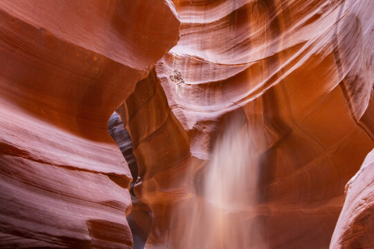 View of sunlight filtering through the narrow, curving sandstone walls of a slot canyon, creating a dramatic display of light and shadow, Page, Arizona, United States.