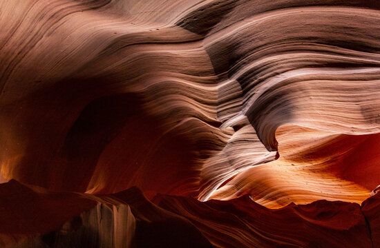 View of swirling sandstone walls, illuminated by soft light and casting deep shadows, creating a mesmerizing dance of color and texture, Page, Arizona, United States.