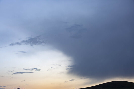View of a dark cloudscape looms over a silhouetted hill against a pale sunset sky, creating a serene yet dramatic contrast, Deosai National Park, Pakistan.