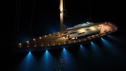 Aerial drone night shot of illuminated luxury yacht with wooden deck anchored in open ocean deep blue sea © aerial-drone