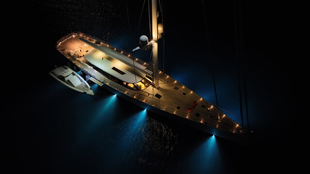 Aerial drone night shot of illuminated sail boat with wooden deck anchored in deep blue Aegan sea