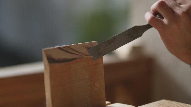 A craftsman meticulously works on a wooden piece, using a sharp chisel to shape the timber. This close-up highlights the precision and skill involved in traditional woodworking.