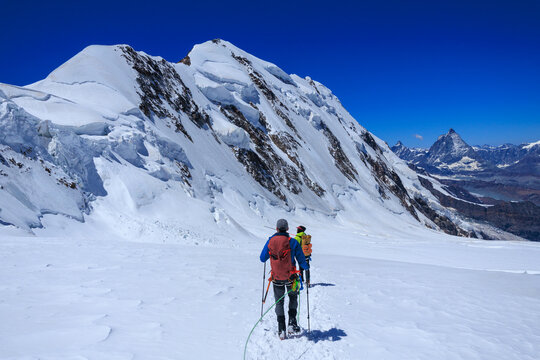 Mountaineers in rope team with crampons descending on glacier Grenzgletscher and mountain panorama with summits Lyskamm and Matterhorn (left to right) in Pennine Alps, Switzerland