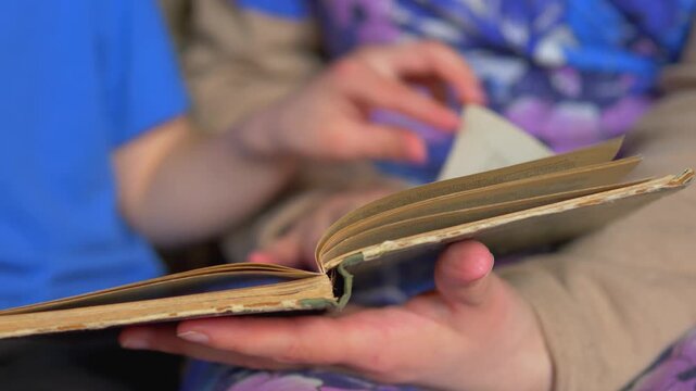 Two People - child and adult - Holding and Leafing Through Worn Vintage Book Together &mdash; Shared Reading, Family Heritage, Intergenerational Knowledge and Storytelling Concept